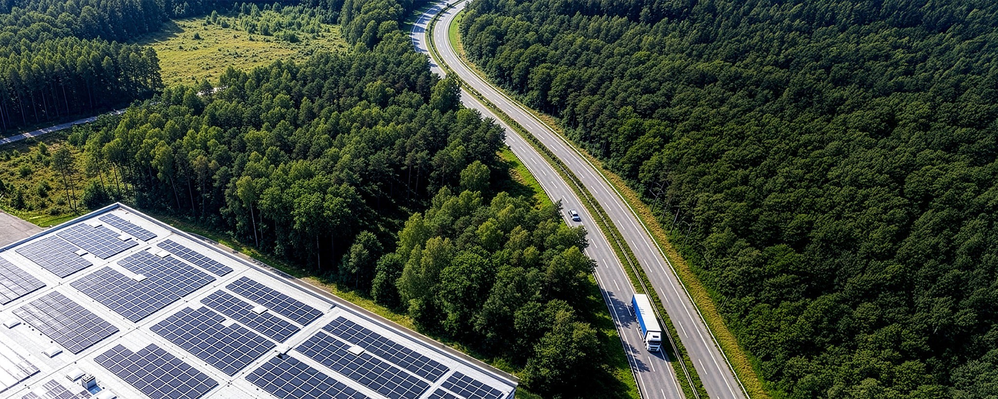 Industrial building with rooftop solar panels next to a forest and highway