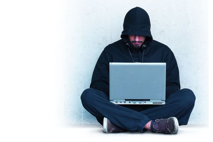 Hacker sits on the floor with a laptop