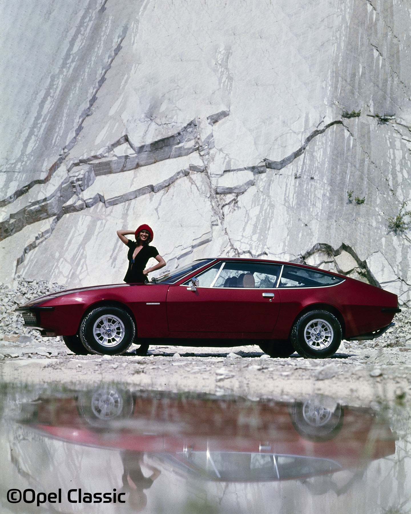 The picture shows an Opel Monza A in front of a stone wall