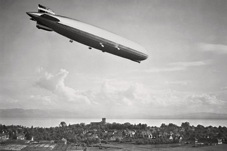 Auf einem Bild in schwarz-weiss fliegt der Zeppelin LZ 127 über Friedrichshafen.