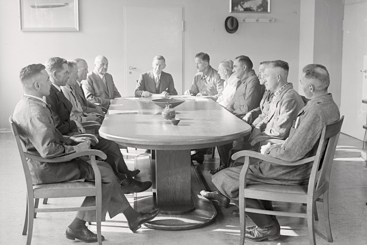 Auf einem Bild in schwarz-weiss aus dem Jahr 1040 sitzen viele Männer an einem Tisch und halten eine Besprechung ab.