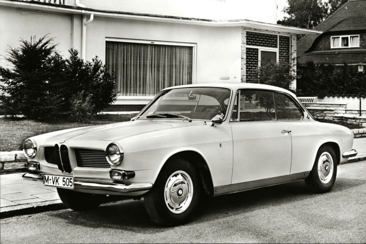 Das Bild in schwarz-weiss zeigt einen BMW 3200 CS schräg von vorne, der vor einem Wohnhaus steht.