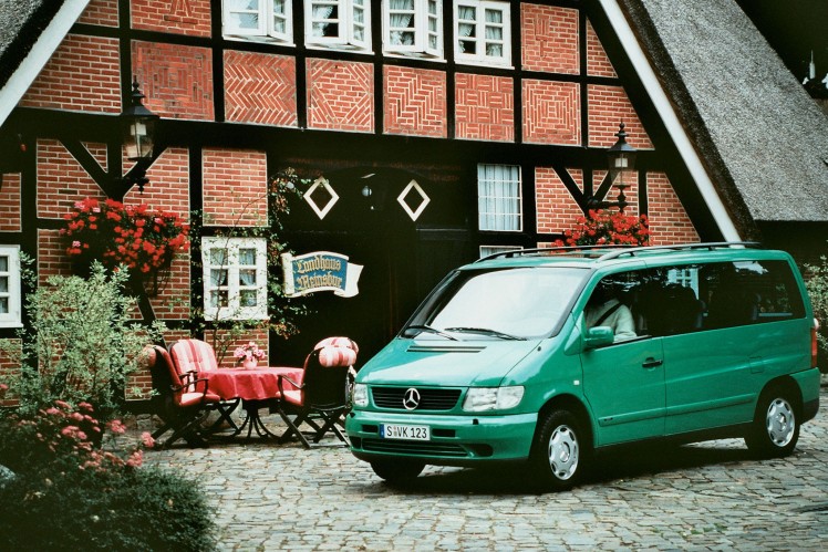 Eine grüne Mercedes-Benz V-Klasse steht vor einem Fachwerkhaus mit Reetdach.