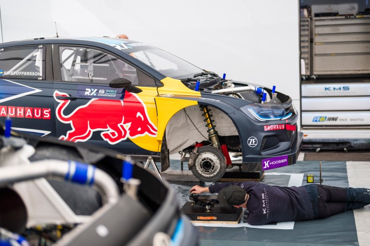 Car in garage lifted off floor with person lying underneath working on it