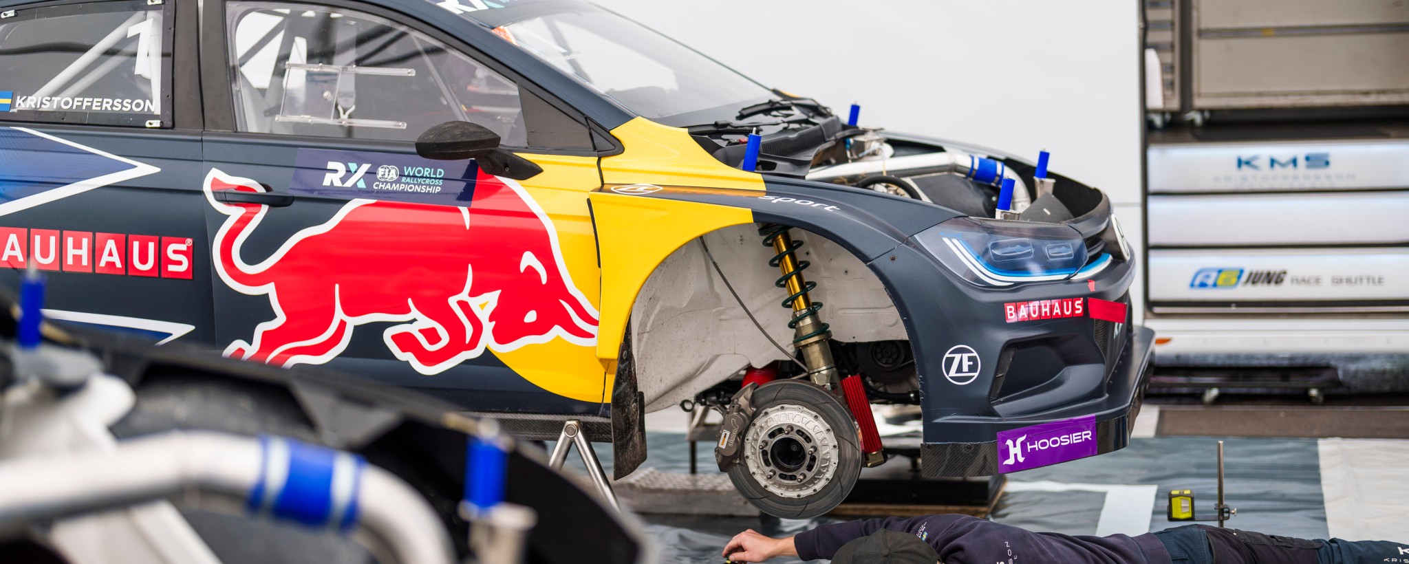 Rally car with wheel off and person lying underneath working on car