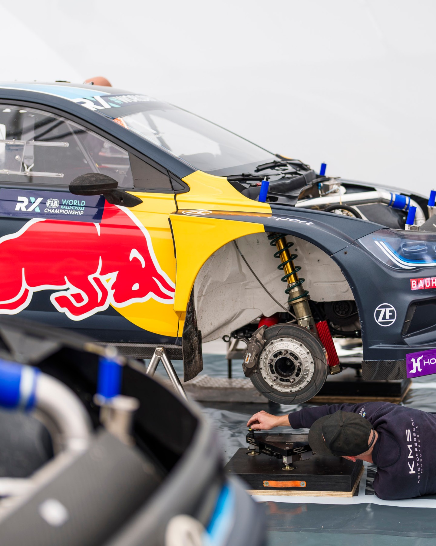 Rally car with wheel off and person lying underneath working on car