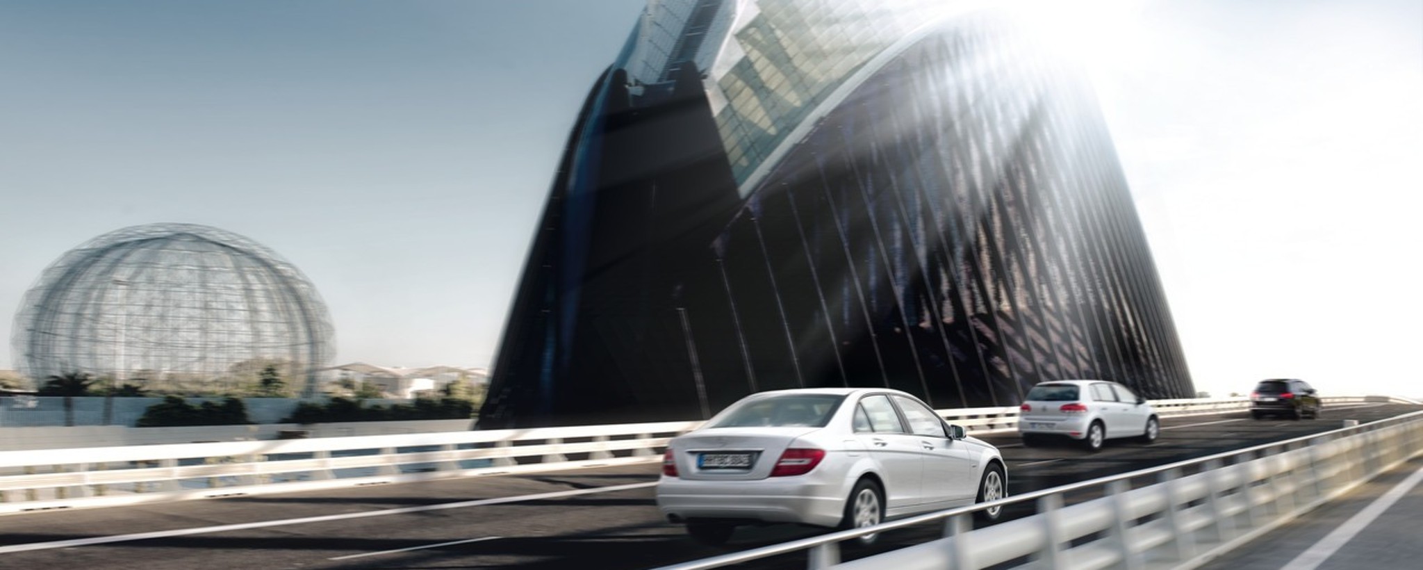 Silver car driving over bridge in bright sunlight