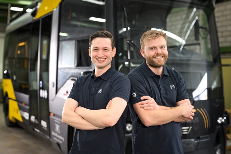 Two men with their arms crossed stand shoulder to shoulder and smile into the camera.
