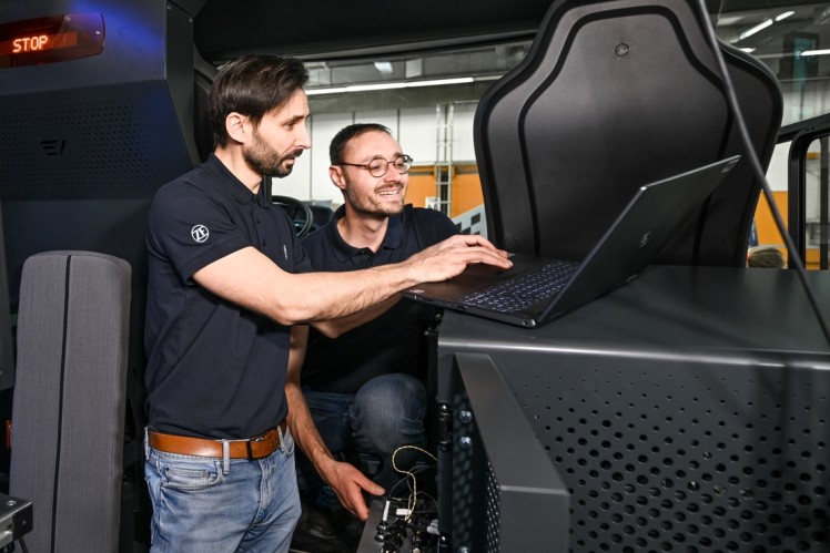 Two men in a vehicle look at a laptop.